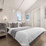 Schlafzimmer mit Bett, Fenster und Holzwandverkleidung. Links Sitzbank mit Felldecke.