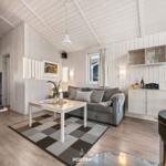 Wohnzimmer mit Sofa, Tisch und Kaminofen. Holzwände und -decke. Fenster mit Vorhang.