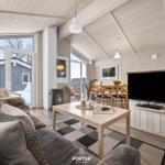 Wohnzimmer mit Sofa, Esstisch und TV. Holzwände und große Fenster.