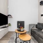 Wohnzimmer mit Sofa, Fernseher und kleinem Tisch mit Obst und Wein.