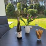 Tisch mit Wein, Tulpen und Knäckebrot auf Terrasse mit Gartenblick.