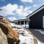 Schwarze Holzhäuser mit weißen Türen und Schnee im Vordergrund.
