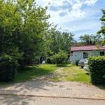 Haus mit Garten, Terrasse und Parkplatz. Umgeben von Bäumen und Sträuchern.