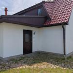 Haus mit weißer Fassade, braunem Dach und Eingangstür. Vor dem Haus befindet sich ein gepflasterter Bereich.