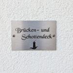 Metalltafel mit Schriftzug und Leuchtturm-Symbol an weißer Wand