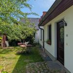 Hinterhof mit Tisch, Stühlen und grünem Rasen. Eingangstür und Fenster mit Pflanzen.