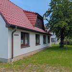 Ein Haus mit rotem Dach und weißen Wänden. Grasfläche und Baum vor dem Gebäude.