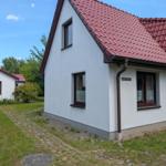 Wohnhaus mit rotem Dach und weißen Wänden, gepflasterte Zugangsweg und grüner Garten.