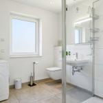 Bathroom with shower, sink, and toilet. Window, washing machine, and sink visible.
