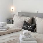 The bed is decorated with pillows and towels. A wall lamp and nightstand are visible.