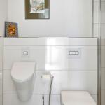 Bathroom with toilet, sink and shower. Wall-mounted rack and pictures on the wall.