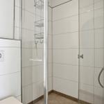 Shower with glass enclosure and showerhead. Toilet with seat and wall mounting.