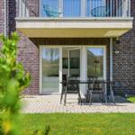 Terrace with table and chairs in front of a house with balcony and glass doors.