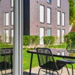Terrace with table and chairs. View of green lawn and brick house.