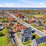 Aerial view of a residential area near the sea with houses, roads, and green spaces.
