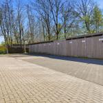 Paved area with wooden garages and trees in the background.