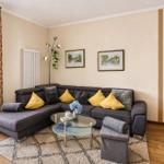 Ein Wohnzimmer mit grauem Sofa, gelben Kissen und Glas-Tisch.
