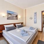 Schlafzimmer mit Doppelbett, Wandbild und Holzboden. Durchgang zu Wohnbereich.