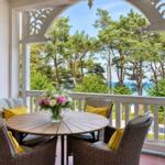 Terrasse mit runden Tisch und Stühlen, Blick auf Bäume und Meer.