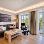 Wohnzimmer mit Sofa, Sessel und Balkon. Blick auf Wald. Holzfußboden und Wandbild.