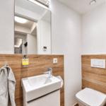 Badezimmer mit Waschbecken, Spiegel und Toilette. Holzwand und graue Handtuch.