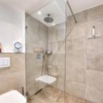 Dusche mit Glaswand, Duschbrause, Toilette und Handtuchhalter.