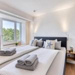 Schlafzimmer mit Doppelbett, Fensterblick auf Wald und gefalteten Handtüchern.