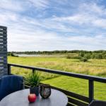 Terrasse mit Tisch, Stuhl und Blick auf Grünfläche und Wasser.