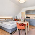 Ein Schlafzimmer mit Doppelbett, Küchenzeile und Esstisch mit zwei orangefarbenen Stühlen.