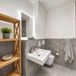 Bathroom with sink, toilet, and shower. Wooden shelf with plant and bowl.