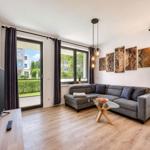 Living room with sofa, glass table, and TV. Large windows with garden view.