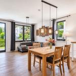 Dining area with wooden table and chairs, living area with sofa and windows.