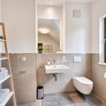 Badezimmer mit Waschbecken, Toilette und Fenster mit Blick auf Bäume.