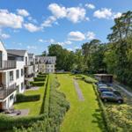 Moderne Apartments mit Balkonen, grüner Rasenfläche und Parkplatz in Waldnähe.