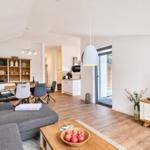Wohnzimmer mit Sofa, Couchtisch und Fernseher. Küche und Essbereich im Hintergrund.