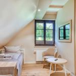 Attic room with bed, chair, and table. Windows and mirror on the wall.