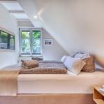 Bedroom with sloped ceiling, window, and bed with pillows and blanket.
