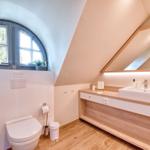 Bathroom with sloped ceiling, sink, and window with view of greenery.