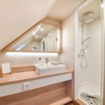 Bathroom with shower, sink, and mirror under sloped ceiling.
