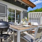 Terrace with table, chairs, grill, and beach chair. House with windows and roof.