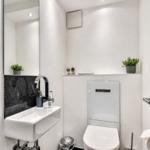 Badezimmer mit Waschbecken, Spiegel und Toilette. Weiße Wände und moderne Einrichtung.