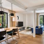 Wohn- und Essbereich mit Holzboden, blauem Sofa und großen Fenstern.