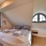 Schlafzimmer mit Doppelbett, Holzboden und zwei Fenstern mit Blick auf die Landschaft.