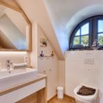 Badezimmer mit Waschbecken, Spiegel und Toilette unter einem Bogenfenster.