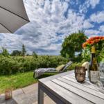 Terrasse mit Tisch, Sonnenschirm und Blick auf grüne Wiesen.