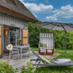 Haus mit Terrasse, Liegestuhl und Strandkorb unter Sonnenschirm.