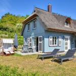 Blue house with thatched roof and garden furniture. Terrace with table and chairs.