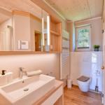 Bathroom with sink, mirror, and toilet. Wooden ceiling and window with view.