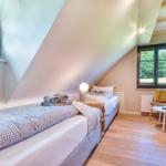 Two beds under sloped ceilings with windows and wooden floor.