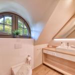 Bathroom with wooden vanity, mirror, and arched window overlooking greenery.